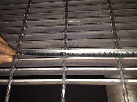 A hand is measuring the cross bar pitch of the welded steel grating.